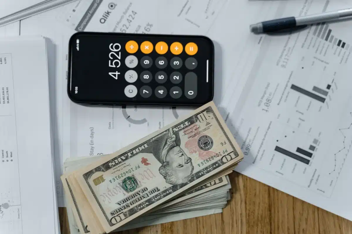 desk with currency spreadsheets and a calculator, anonymous hands pointing at a chart