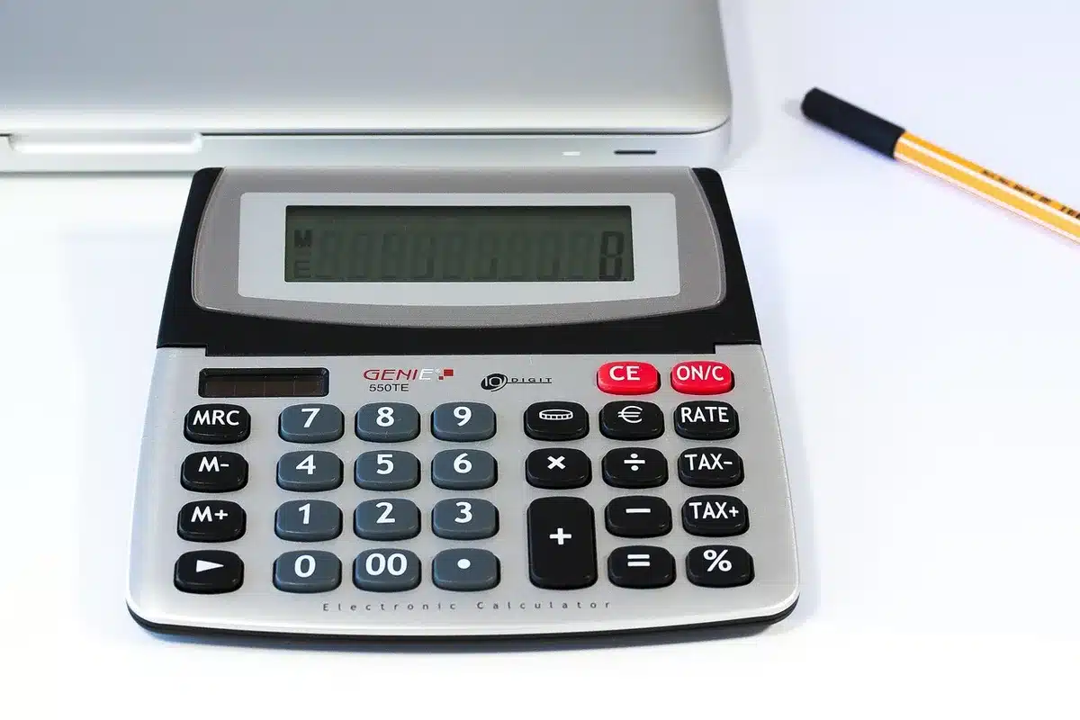 Close-up of hands writing numbers on a financial ledger beside a calculator and scattered blurred coins in the background
