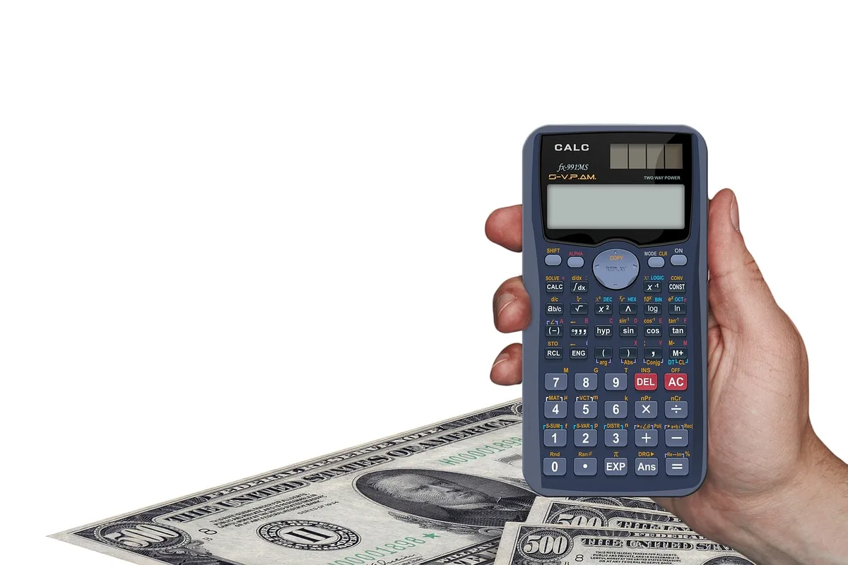 close-up of a calculator and financial notes on a desk with a blurred gold coin in the background